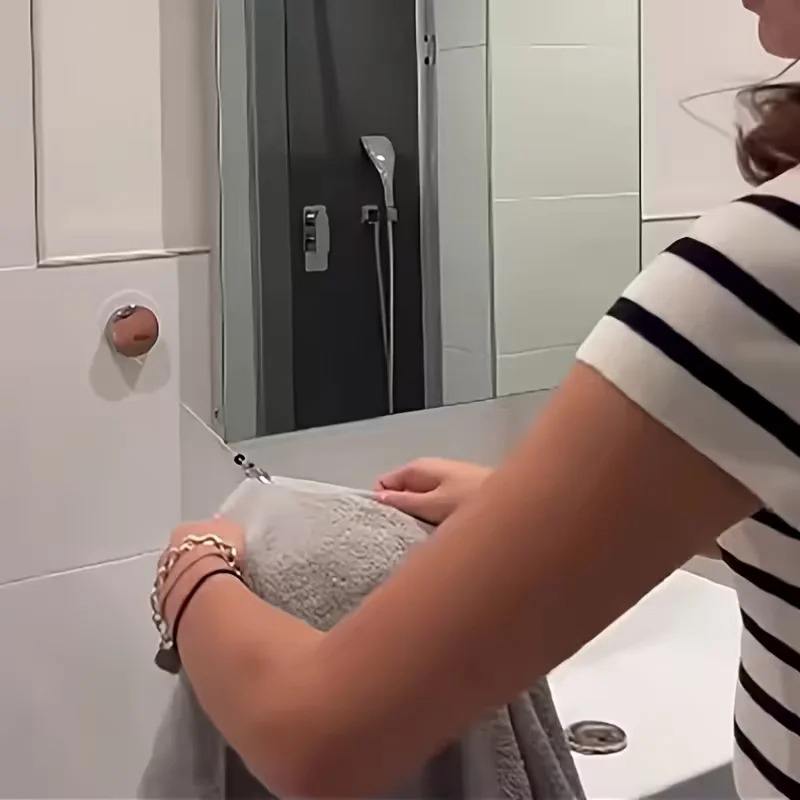 Person installing a retractable adhesive towel rack on a bathroom wall.