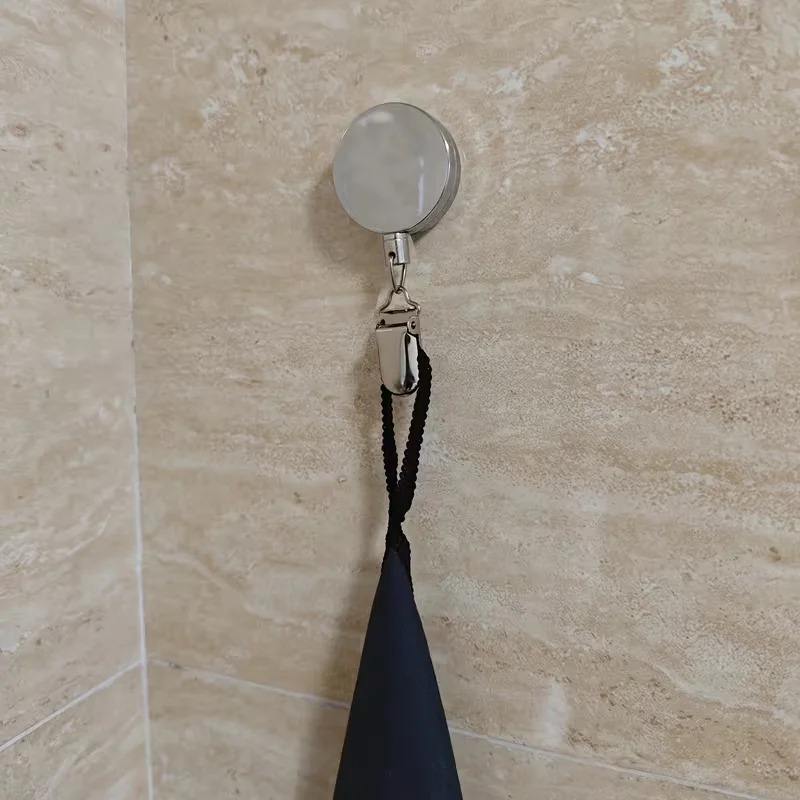 Retractable adhesive towel rack mounted on a tiled wall holding a dark towel.